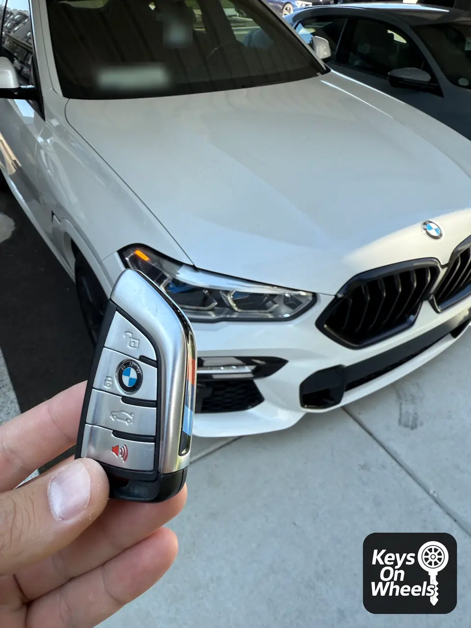 BMW smart key held up next to the headlight of a white BMW in Meridian