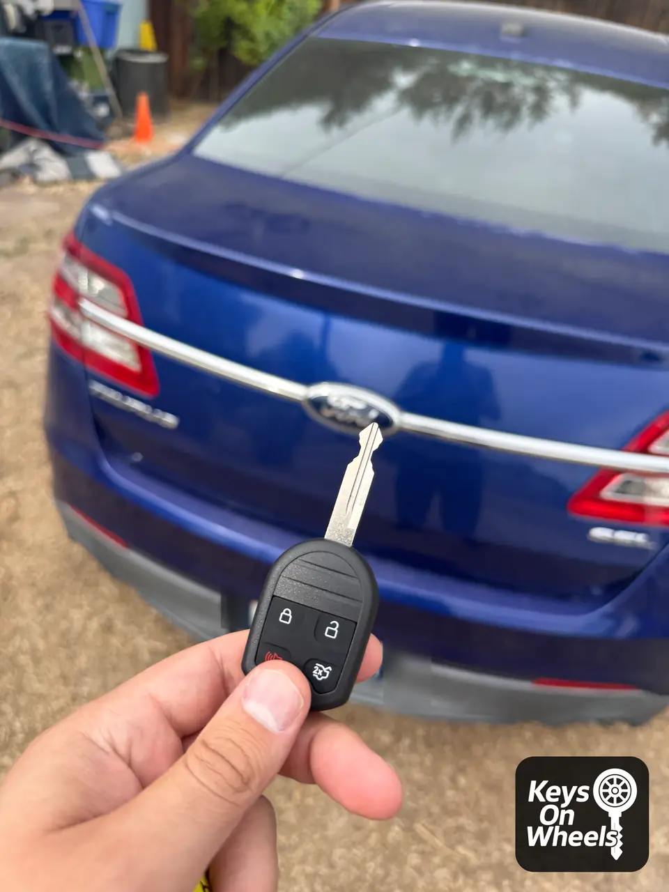Ford remote-head key with lock, unlock, panic and trunk buttons, behind a blue Ford Taurus in the Boise area