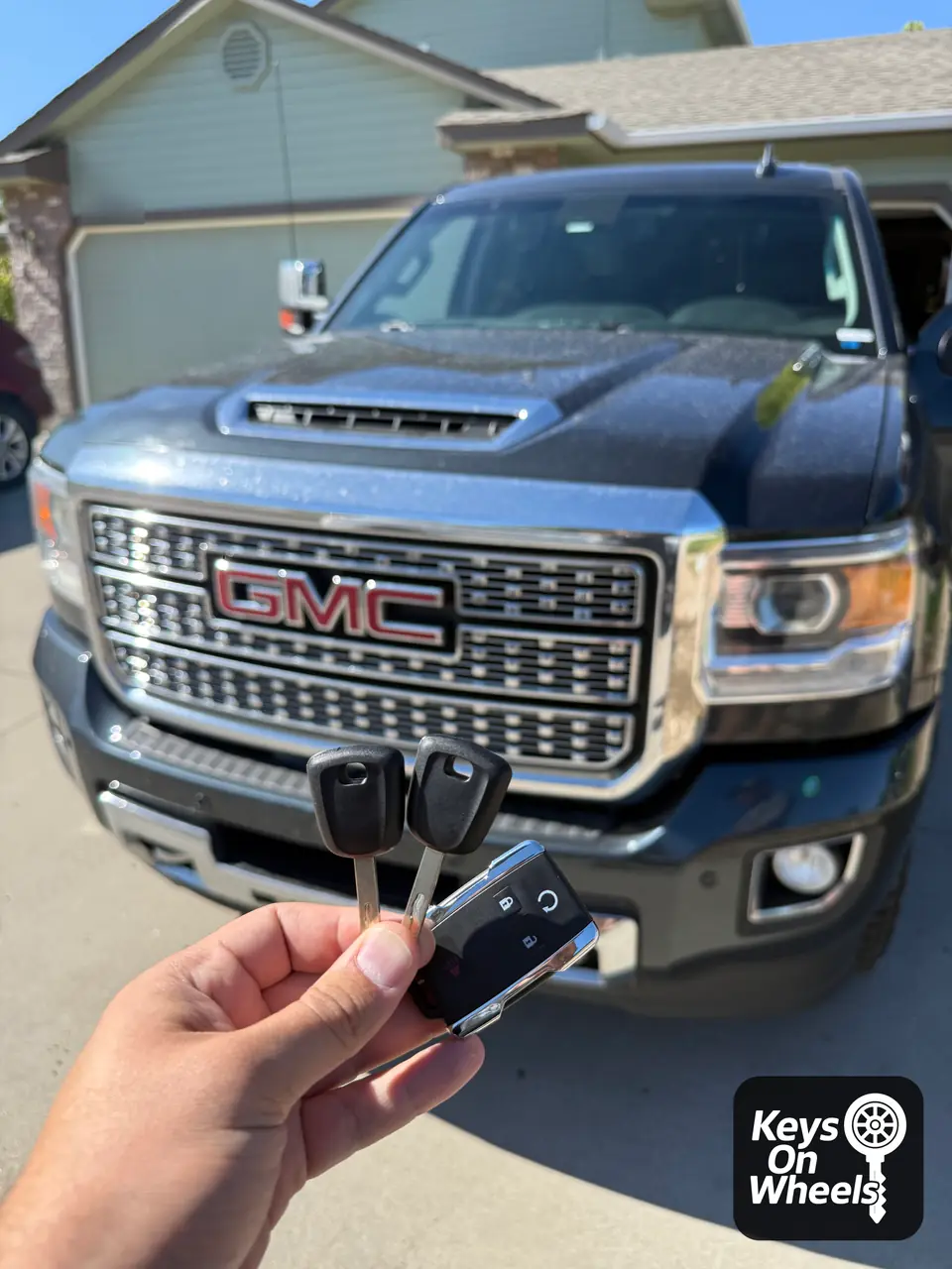 Two chip keys and a remote with a remote-start button, held in front of a GMC Sierra pickup in Nampa