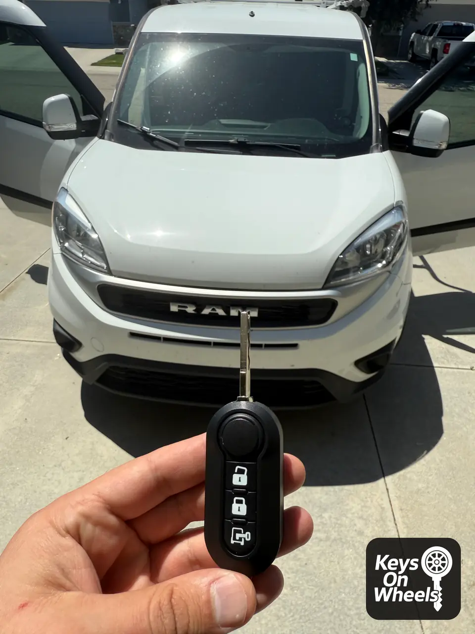 Flip key with its blade folded out, held in front of a white Ram ProMaster City