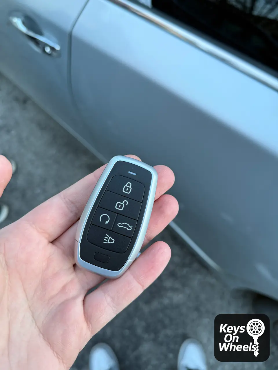 Five-button smart key with remote start, held next to the door of a silver car