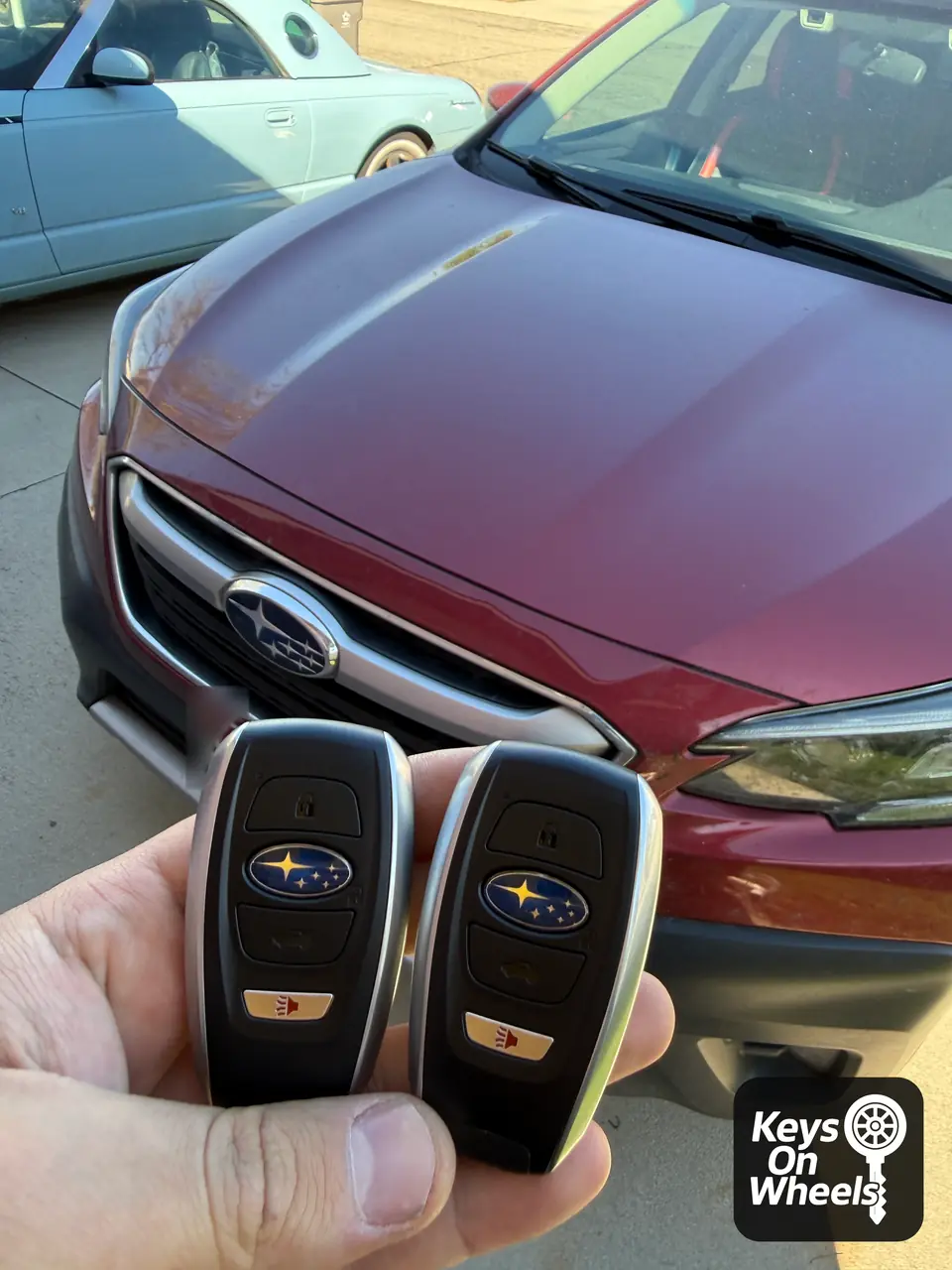 Two Subaru smart keys held in front of a red Subaru in the Boise area